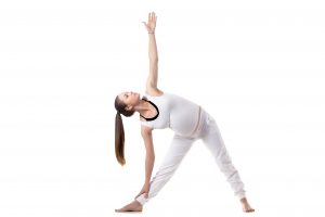 Full length portrait of young pregnant fitness model in white sportswear doing yoga or pilates training, standing in Triangle pose, Trikonasana, white background, studio shot, isolated